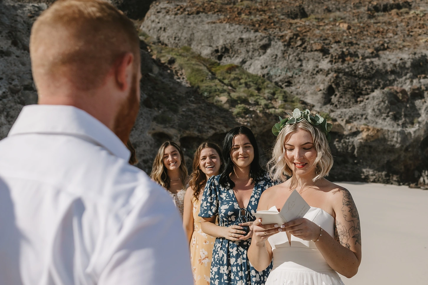 bride reading vows to the groom and her friends are behind her excited. 