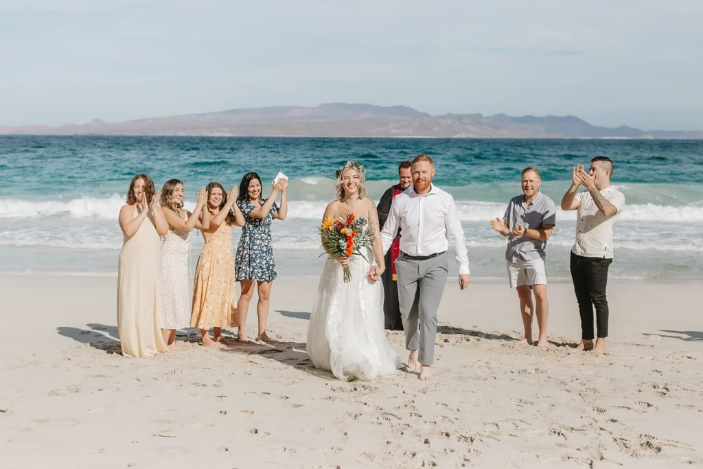 couple walking holding hands after their elopement ceremony and their closest guest are celebrating in a beautiful beach in los barrels, Baja California Sur. 