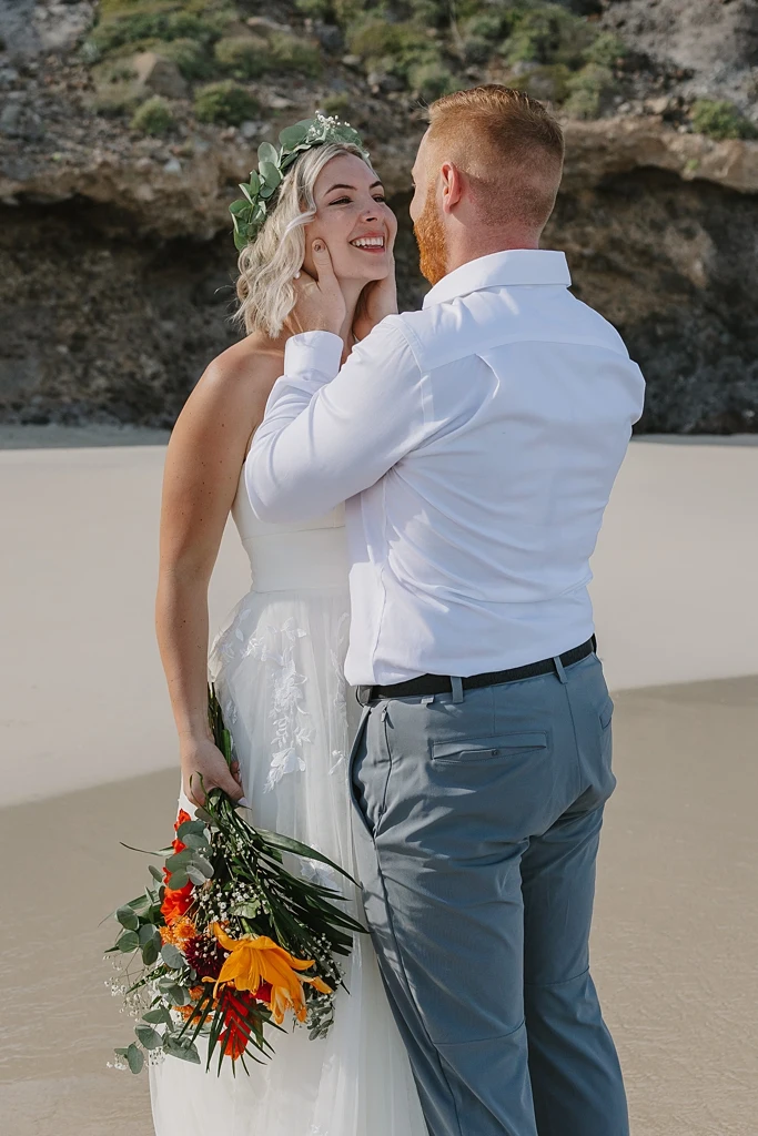 couple eloping in a beach, hugging and behind is a mountain. 