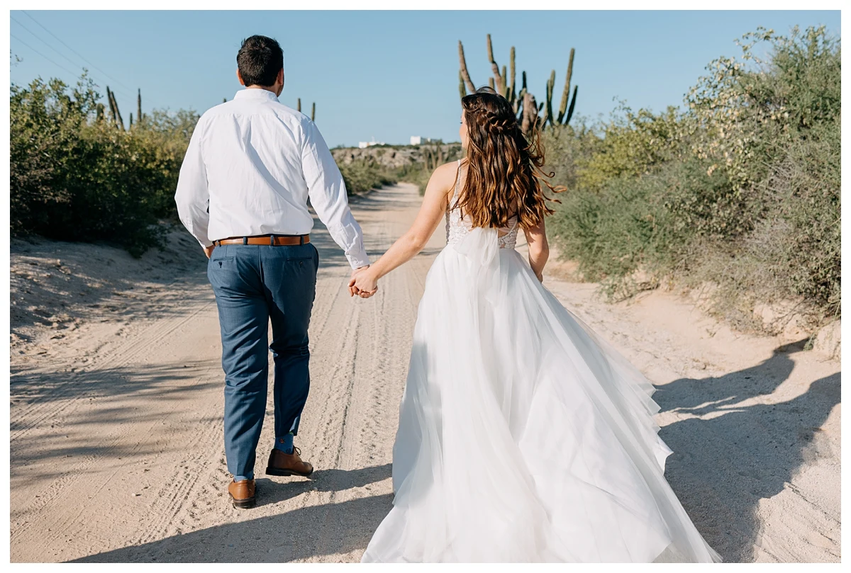 couple-photos-in-baja bride & groom holding hands walking together surrounded by cacti in Baja.